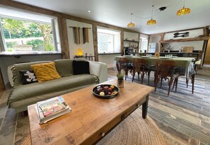 A cozy living room with a sofa, a coffee table with a bowl of fruit, and a dining area with chairs and a table. - Newly Renovated Old Mill in Douarnenez (Douarnenez)