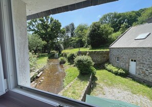 Ein Steinhaus mit einem kleinen Bach, umgeben von Grünflächen und Bäumen.