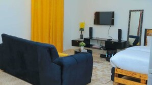 Ein Zimmer mit einer Couch, einem kleinen Tisch mit Pflanze, einem Fernseher und einem Spiegel an der Wand.