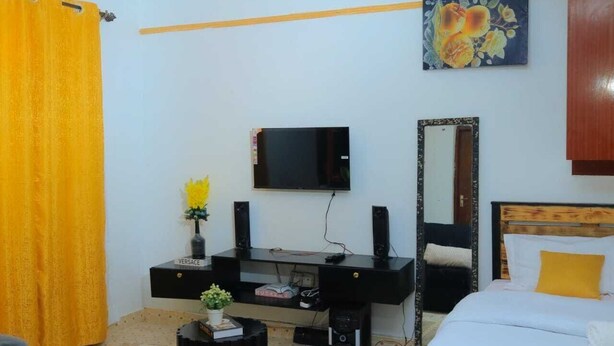 Ein Schlafzimmer mit einem Bett, einem Schreibtisch mit Fernseher, einem Spiegel und einem gelben Vorhang.