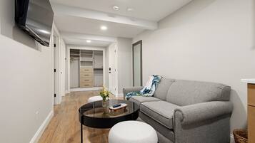 A modern living room with a sofa, a round coffee table, a TV mounted on the wall, and a walk-in closet.