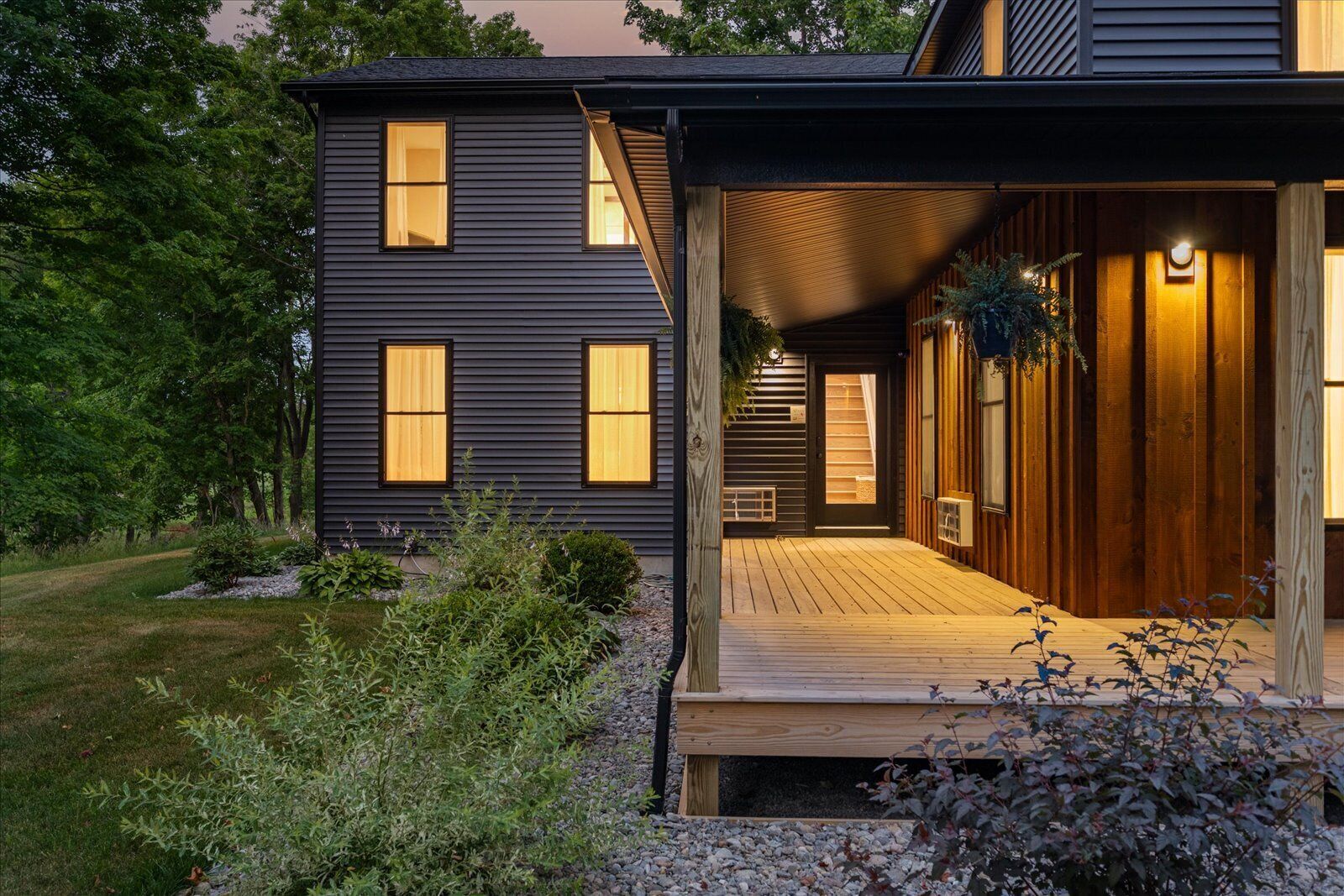 Una casa moderna con terraza de madera, ventanas amplias y un jardín bien cuidado.