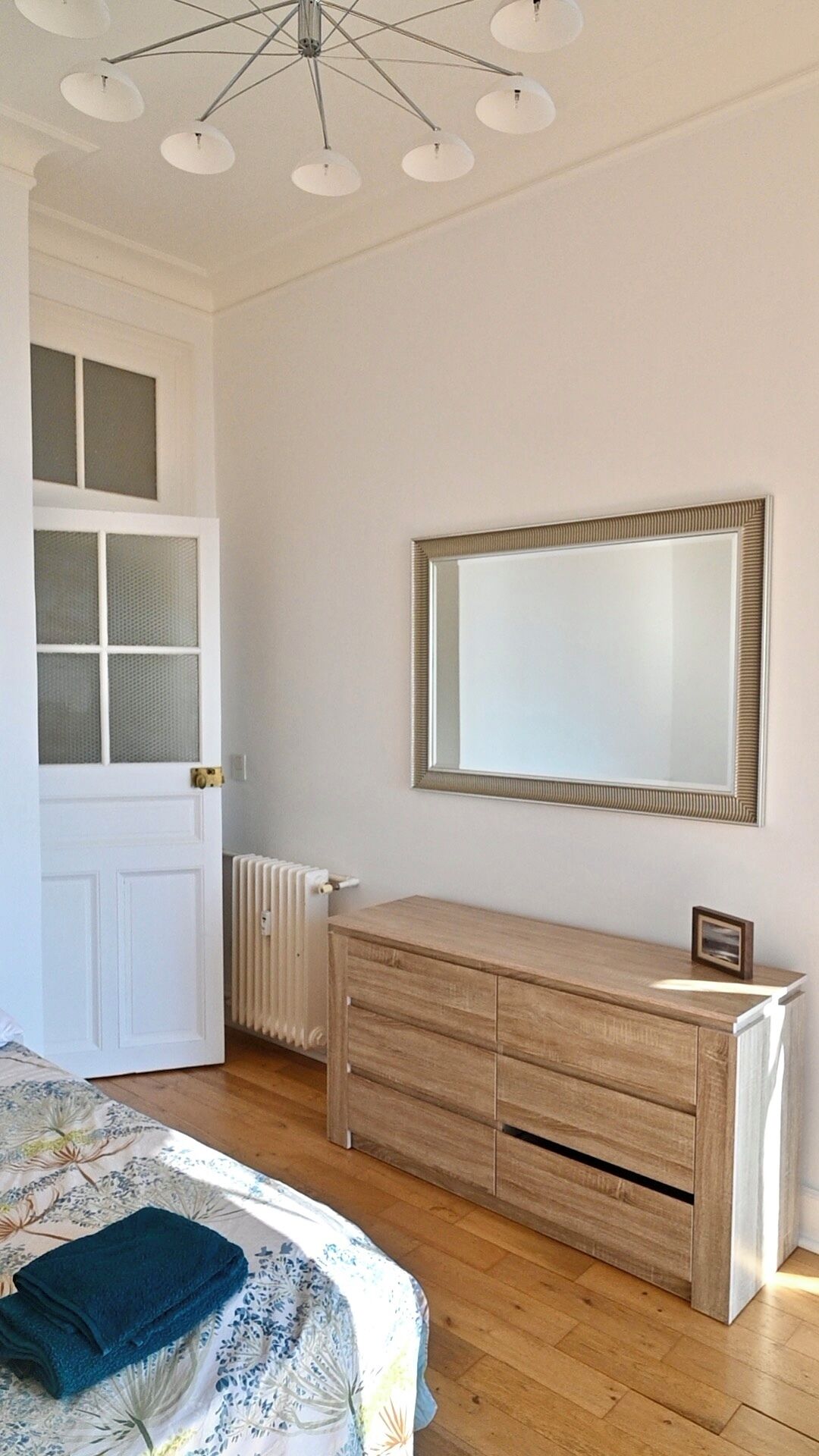 A bedroom with a bed, a dresser, a mirror, and a radiator.