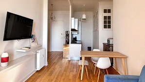 Un saló modern amb un televisor de pantalla plana, un sofà blau, una taula de centre de fusta i una zona de menjador amb una taula i cadires de fusta.