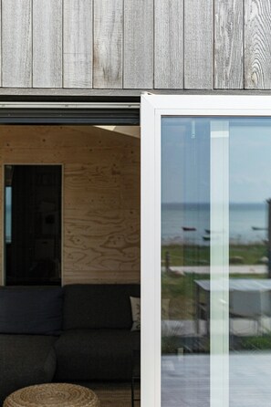 Un intérieur moderne avec un mur en bois, une porte vitrée donnant sur l’extérieur et un canapé de couleur sombre.