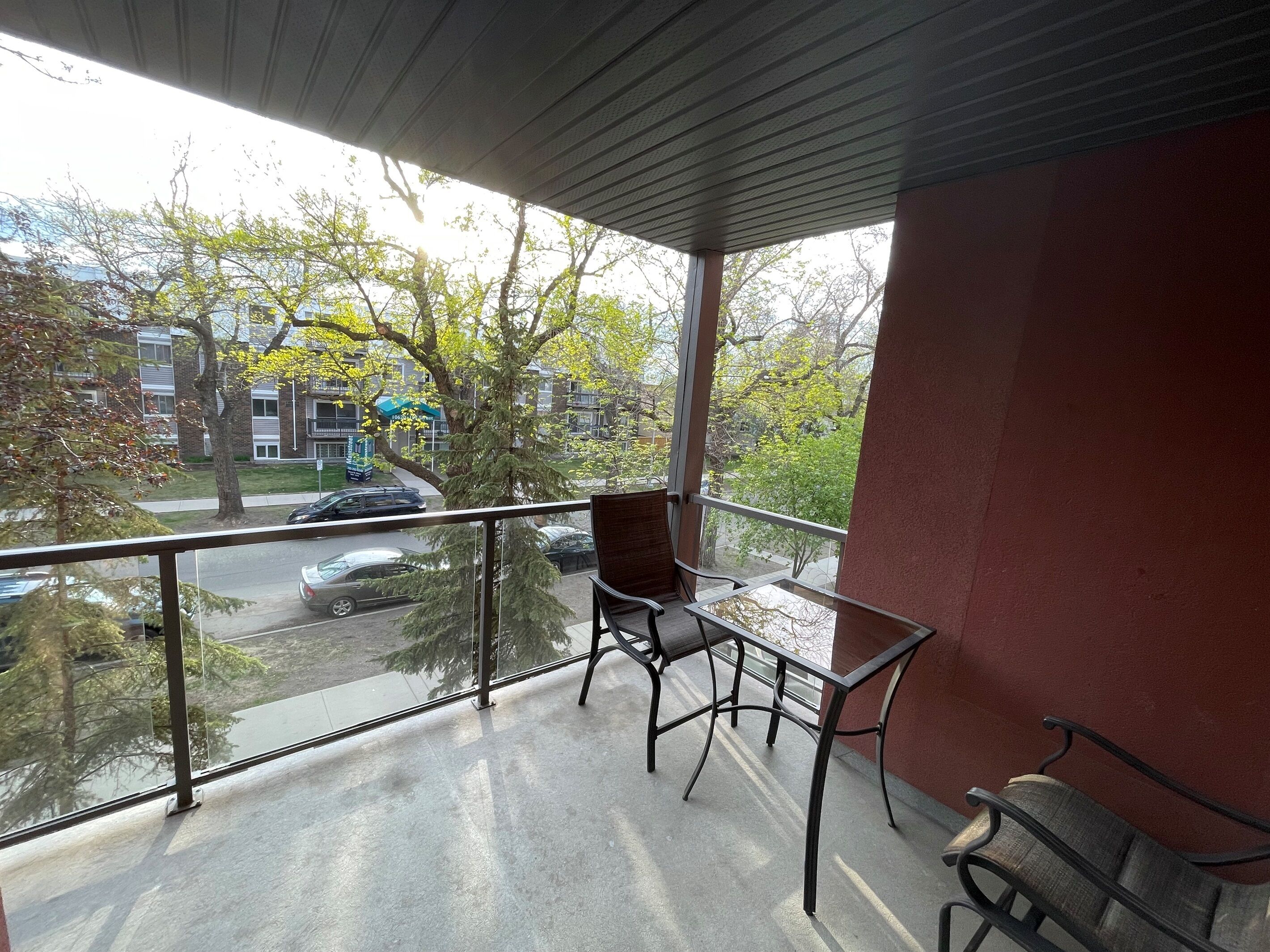 Un balcone con ringhiera in vetro, due sedie e un tavolo.