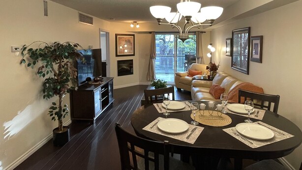 A dining area with a round table set for four, a television, and a sofa in the background. - Times Square Next To Rogers Place #205 (EDMONTON)
