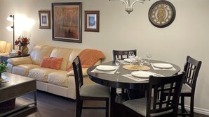 A dining area with a round table, chairs, and a chandelier. There is a sofa and a lamp in the background. - Times Square Next To Rogers Place #205 (EDMONTON)
