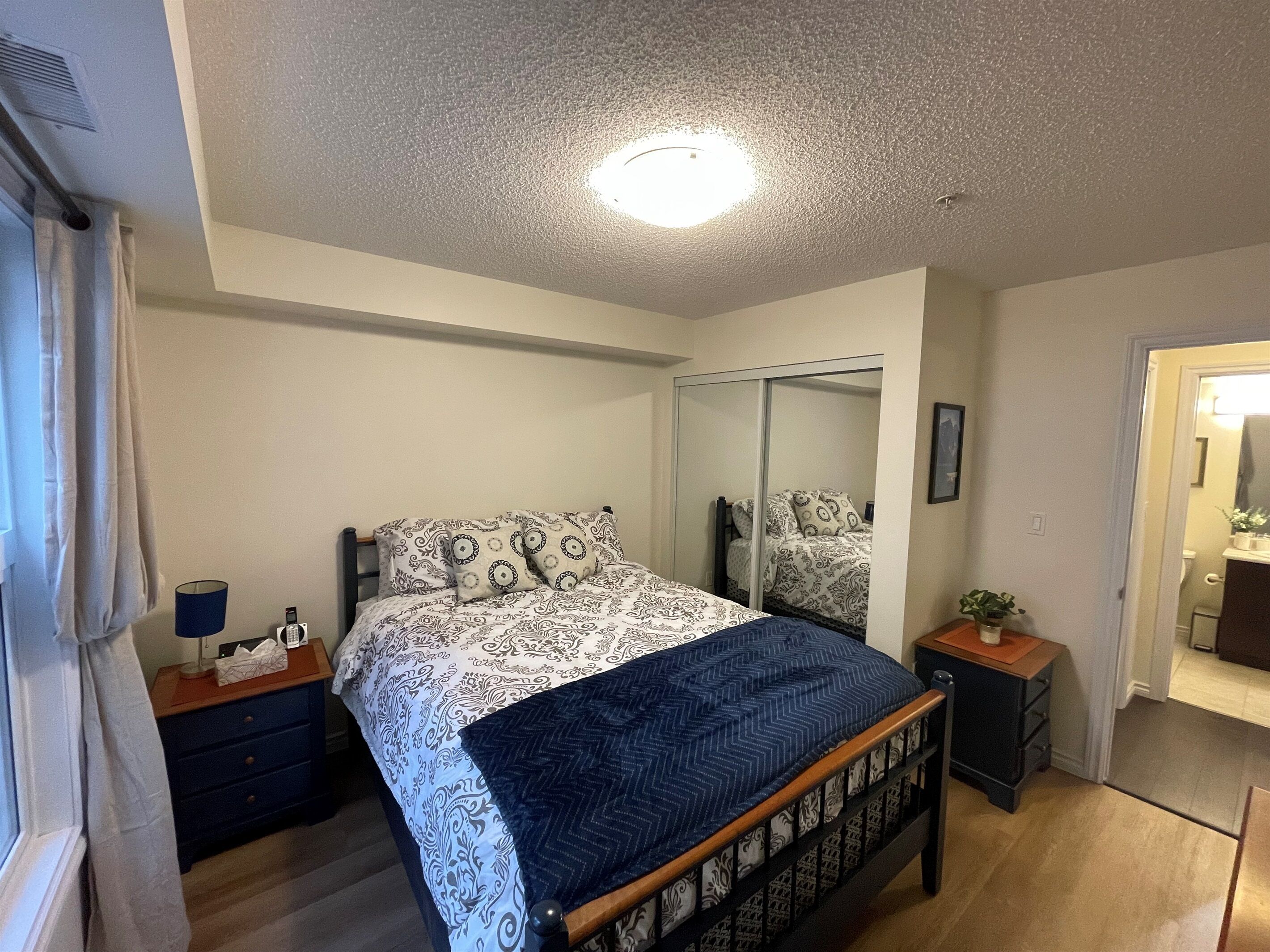 A bedroom with a bed, a bedside table, a nightstand, a mirror, and a wardrobe.