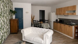Sala de estar com sofá branco, mesa de centro de vidro e área de cozinha com armários de madeira.