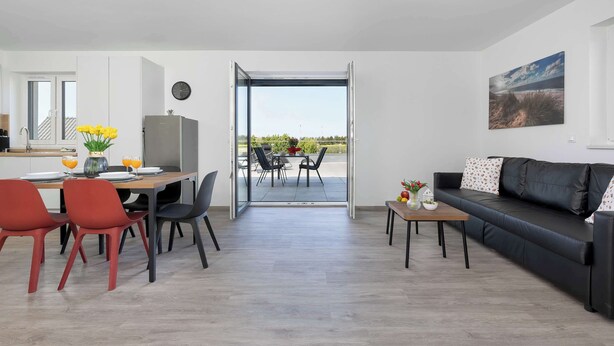 Un espace de vie moderne comprenant un coin repas, un canapé et une vue sur une terrasse extérieure, accessible par une porte vitrée.
