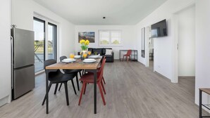 Une cuisine moderne équipée d’une table à manger, de chaises, d’un réfrigérateur et d’un téléviseur fixé au mur.