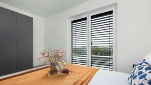 Une chambre à coucher comprenant un lit, une table de chevet, une commode et une fenêtre avec des stores.