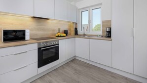 Une cuisine moderne avec des armoires blanches, un plan de travail en bois, un four encastré et une fenêtre.