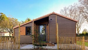 Eine kleine Holzhütte mit einer dunklen Tür, einer kleinen Veranda und einer Schotterzufahrt.