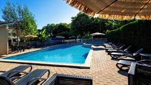 Ein Swimmingpool mit Liegestühlen und Sonnenschirmen, umgeben von Grünflächen.