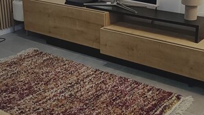 Ett modernt vardagsrum med en platt-TV, ett möblemang i trä för underhållningssystemet och en mönstrad matta.