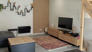 Ett modernt vardagsrum med en platt-TV, en trätrappa och en mönstrad matta.