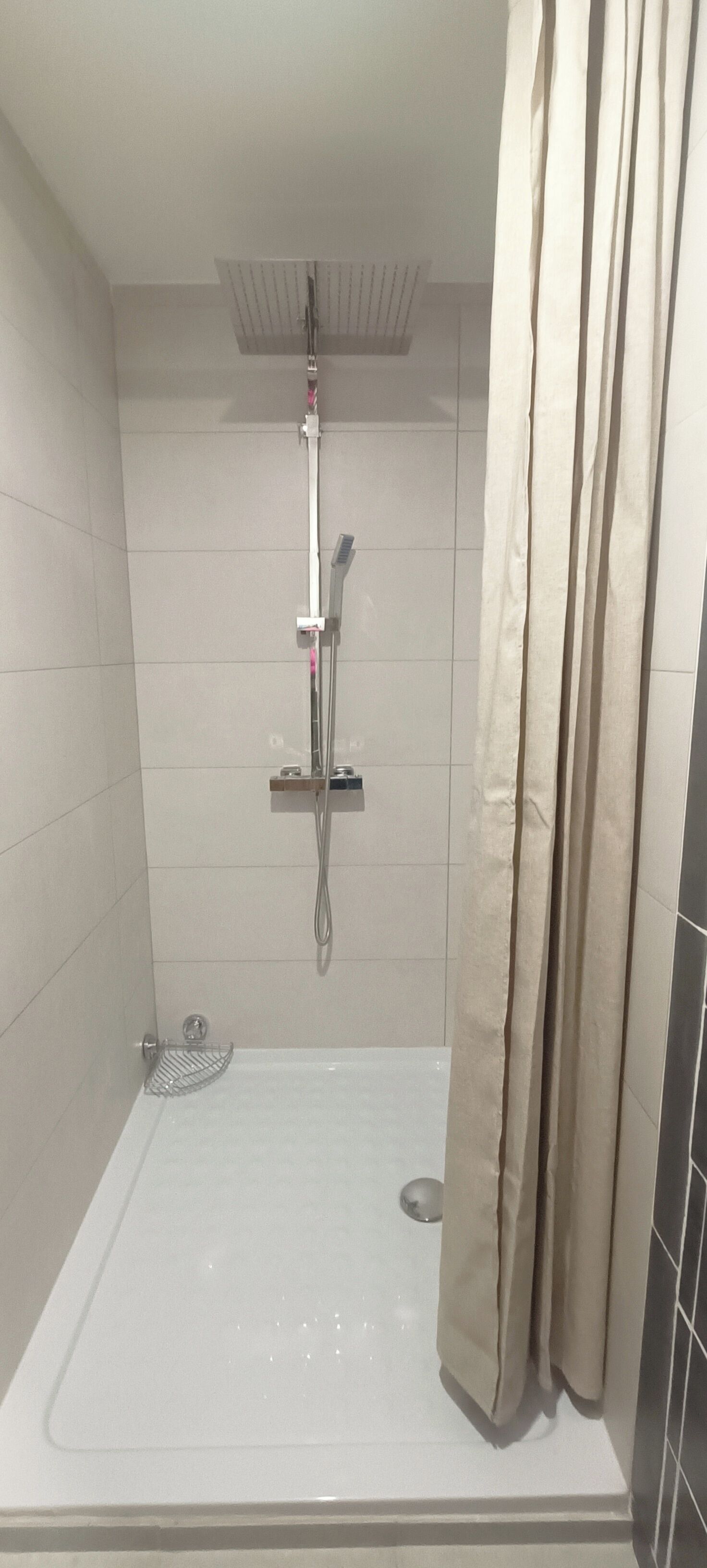 Une douche moderne dotée d’un pommeau de douche à main, d’un robinet mural et d’un receveur de douche.