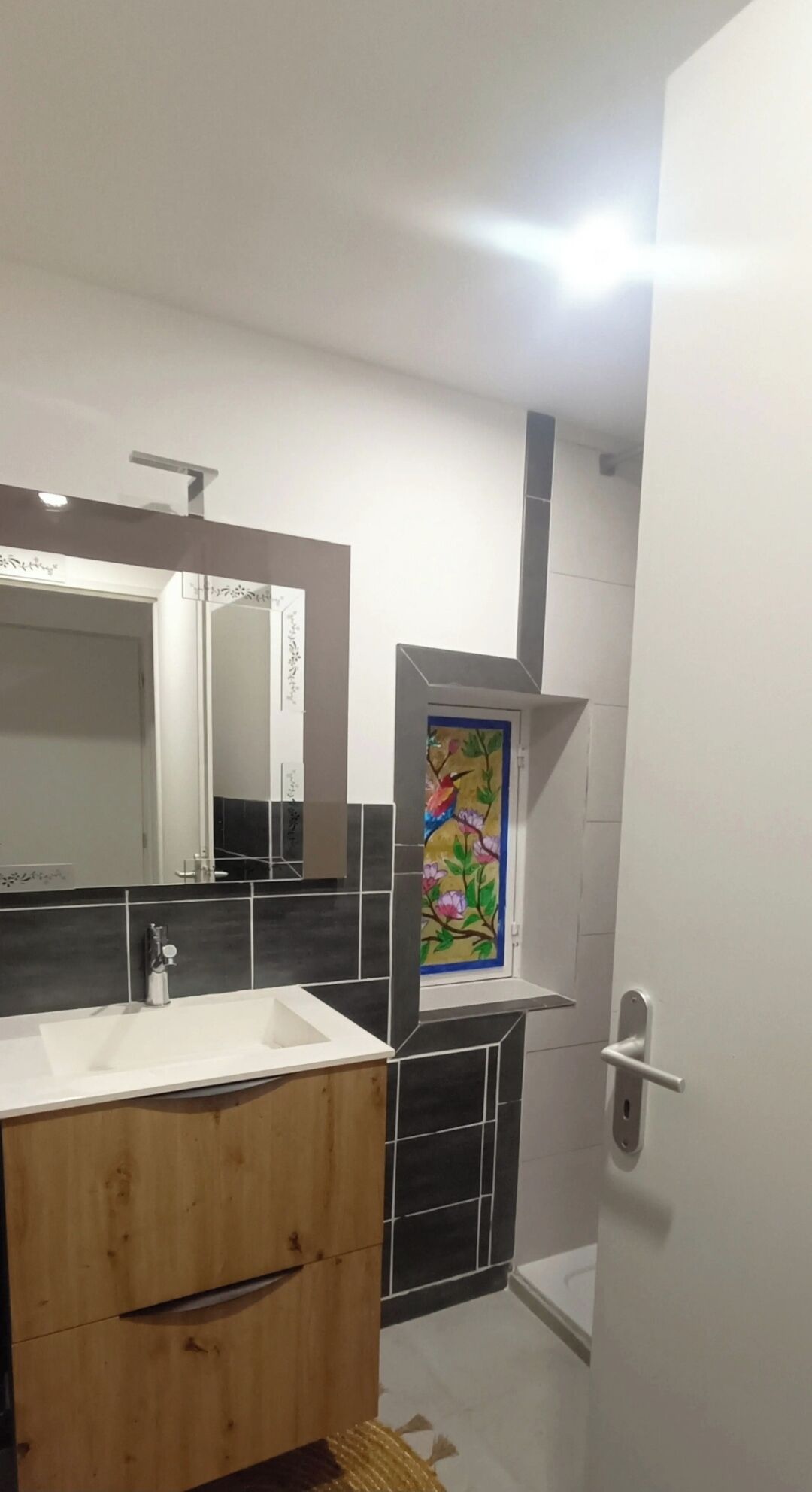 A bathroom with a wooden vanity, a large mirror, a tiled backsplash, and a decorative painting.