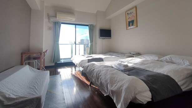Ein Hotelzimmer mit zwei Betten, einem Fernseher, einem Sessel und einem Fenster mit Vorhängen.