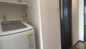 Ein Waschbereich mit einer Waschmaschine, einem Regal mit einer Kiste und einer Tür zu einem anderen Raum.