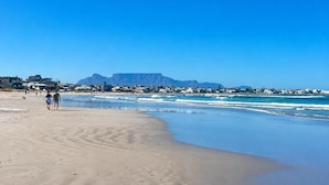 Une plage avec un ciel dégagé, une montagne en arrière-plan et quelques personnes qui se promènent.