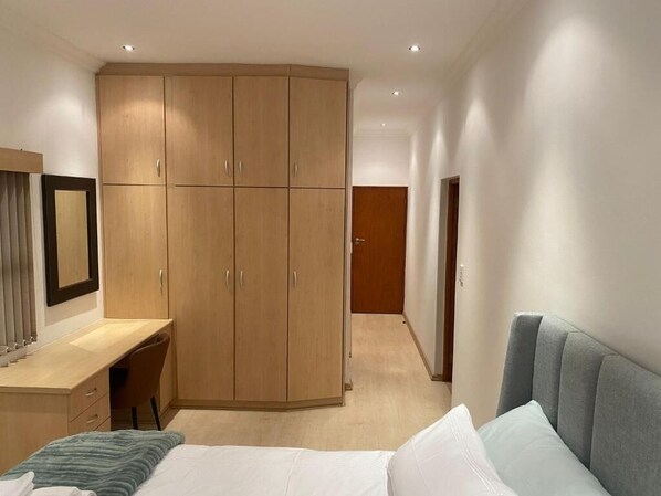 A bedroom with a bed, a desk, and a wardrobe.