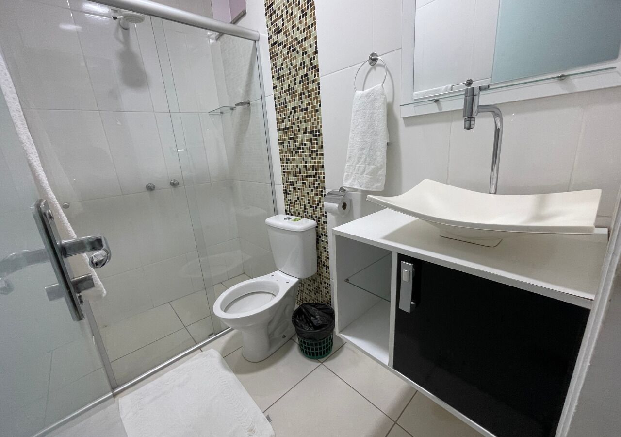A modern bathroom with a glass shower enclosure, a white toilet, a sink with a black cabinet, and a tiled backsplash.