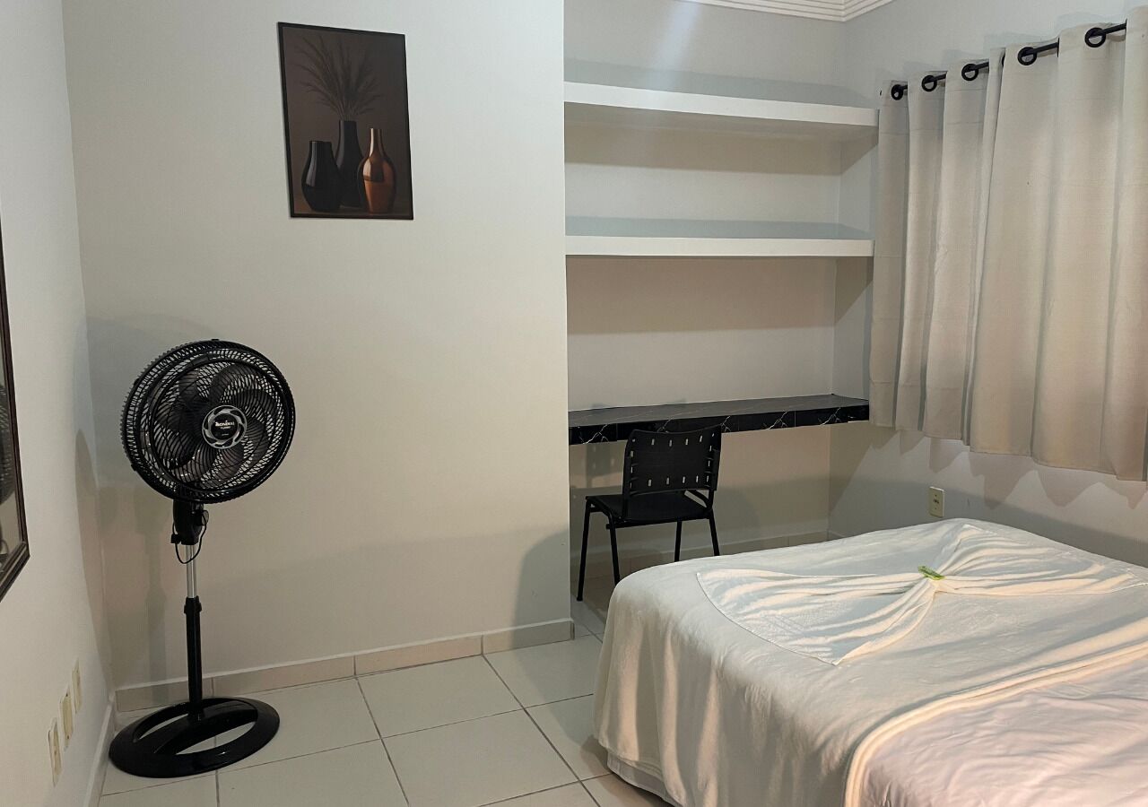 Une chambre à coucher avec un lit, un ventilateur sur pied, un bureau et une chaise.