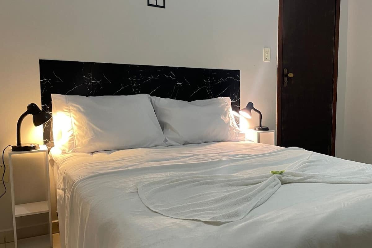 A neatly made bed with white linens, two bedside lamps, and a dark headboard.