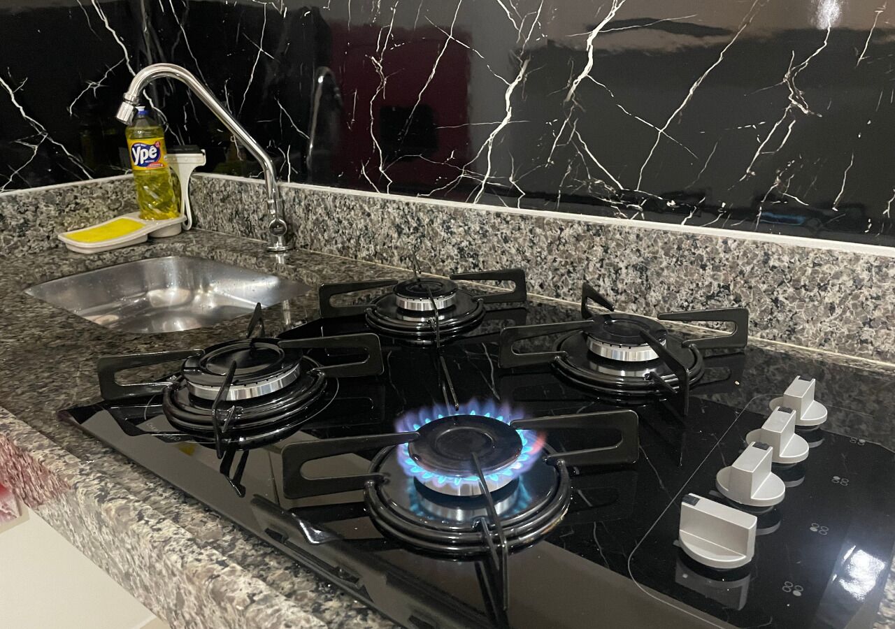 Una cocina con estufa a gas, un lavamanos y una botella de detergente.