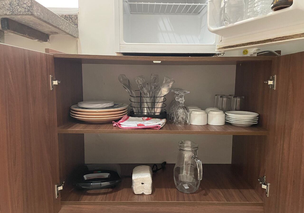 Cozinha com armários de madeira, micro-ondas e diversos utensílios e louças.