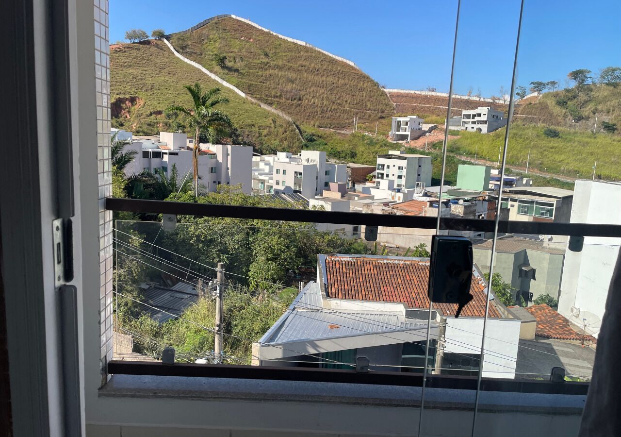 Vista des d'una finestra amb un paisatge de vessant amb edificis, cel clar i línia elèctrica.
