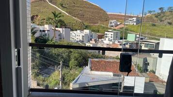 Vista des d'una finestra amb un paisatge de vessant amb edificis, cel clar i línia elèctrica.