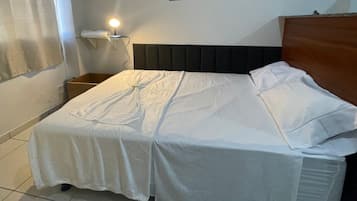 Un letto singolo con copriletto bianco, un comodino con una lampada e una parete con quadri.