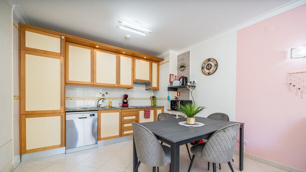 Cozinha moderna com armários de madeira, máquina de lavar louça e área de jantar com mesa e cadeiras.