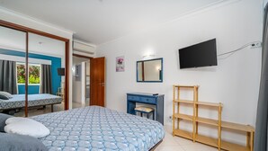 Quarto com cama, escrivaninha, televisão e janela com cortinas.