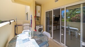 Uma varanda com mesa, cadeiras, máquina de lavar roupa e porta de vidro deslizante que dá para um pátio.