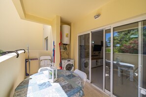 A balcony with a table, chairs, a washing machine, and a sliding glass door leading to a patio area. - 'Casinha Marachique' Apartment with Shared Pool, Wi-Fi, and Air Conditioning (Alvor)