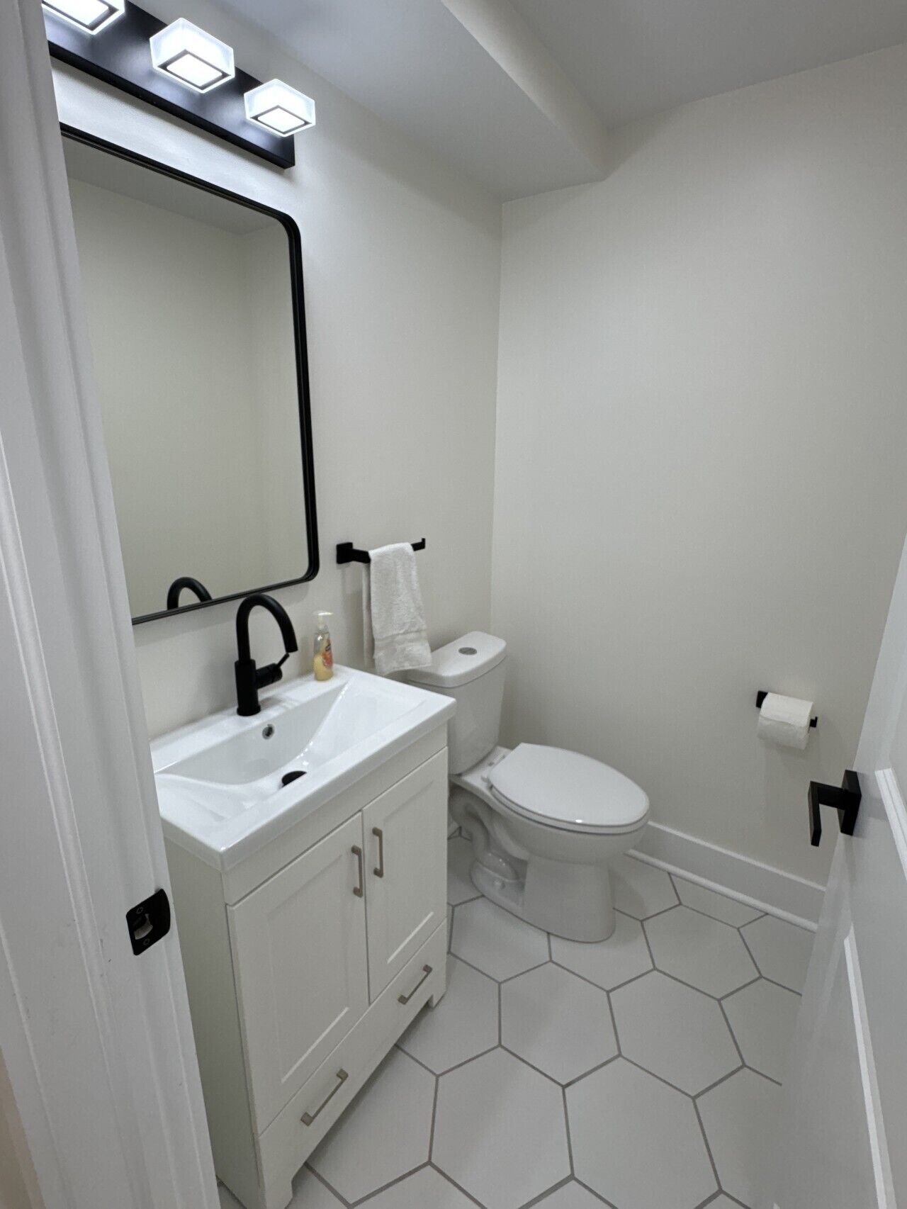 A bathroom with a white sink, mirror, toilet, and hexagonal floor tiles.