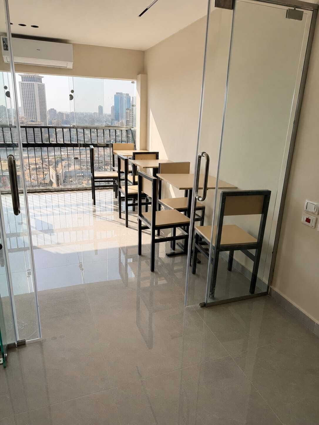A modern room with a glass partition, a city view, and a balcony with chairs.