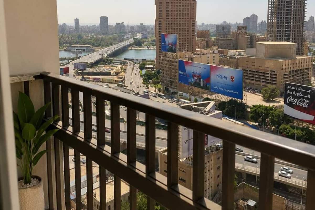 A cityscape with a view of a river, a construction site, and several buildings including a hotel with a large blue sign.