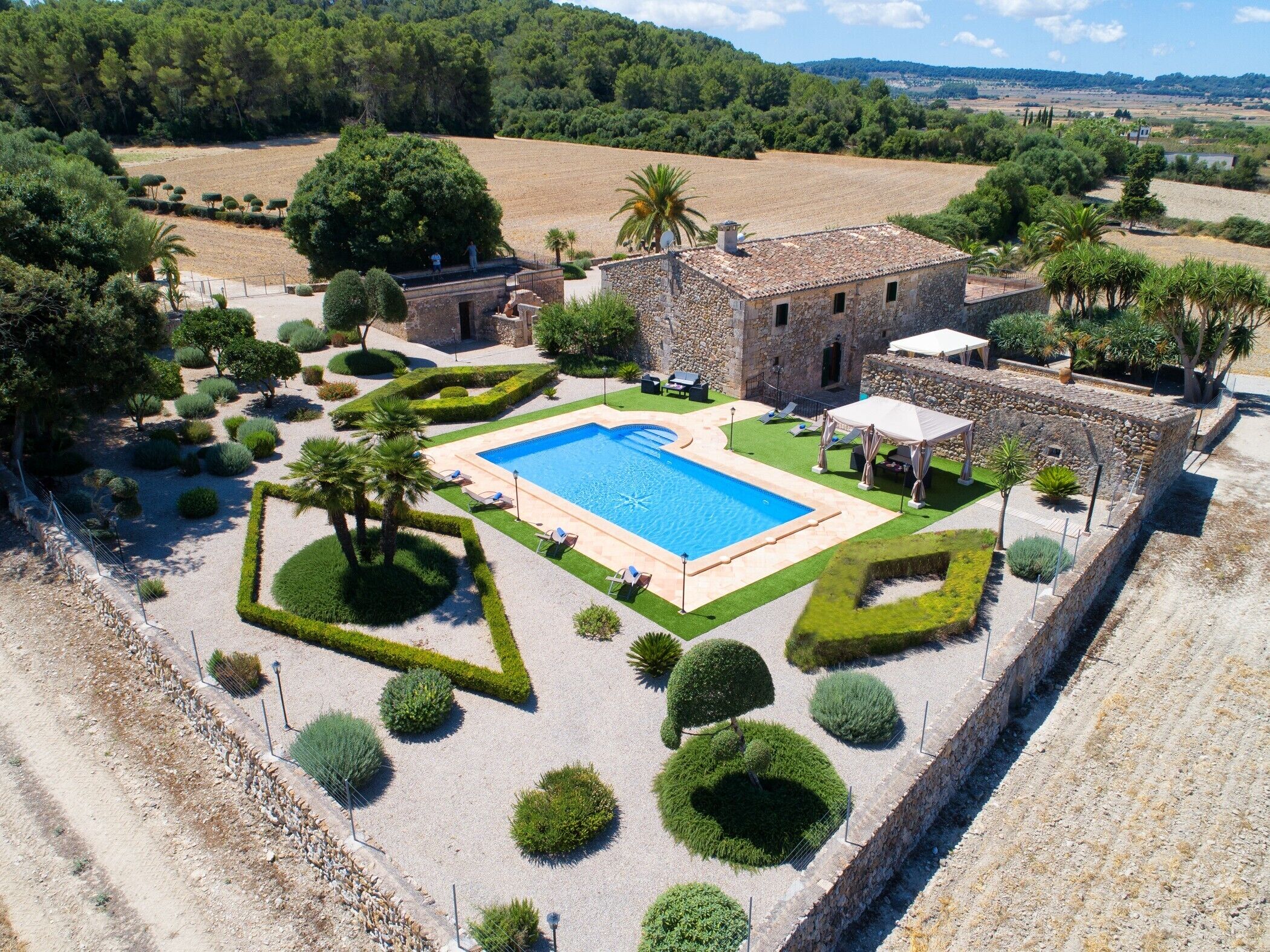 An aerial view of a property with a swimming pool, stone building, and landscaped garden.
