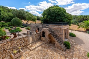 A stone bridge with a metal railing, surrounded by a garden with various shrubs and trees. - Holiday Home 'Finca Son Roig' with Mountain Views, Wi-Fi and Air Conditioning (Sant Joan)