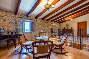 A rustic interior with stone walls, wooden beams, a dining area with chairs and a table, and a staircase with a railing. - Holiday Home 'Finca Son Roig' with Mountain Views, Wi-Fi and Air Conditioning (Sant Joan)