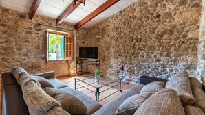 Ein Zimmer mit Steinwänden, einer Couch, einem Fernseher und einem Fenster mit Rollläden.