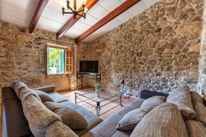 A stone-walled room with a sofa, a TV, and a window with shutters. - Holiday Home 'Finca Son Roig' with Mountain Views, Wi-Fi and Air Conditioning (Sant Joan)