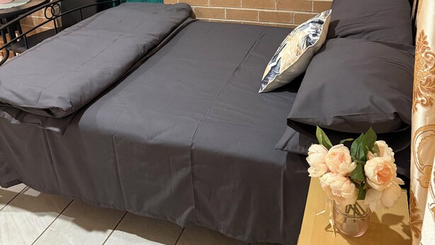 A bed with grey bedding, a vase with flowers, and a brick wall in the background. - Separate private room In Sydney region (Hebersham)