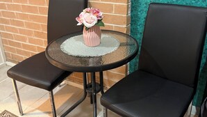 A small round table with a pink vase of flowers, two black chairs, a brick wall, and a green patterned wall. - Separate private room In Sydney region (Hebersham)
